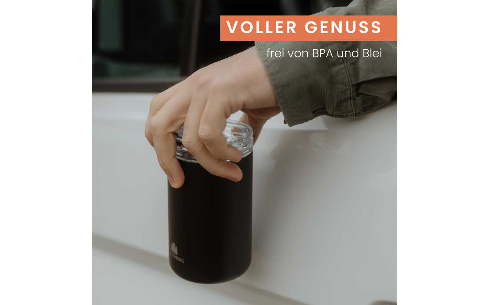 Hand hält einen schwarzen Becher mit transparentem Deckel vor einer weißen Autotür; oben ein rotes Banner mit dem Schriftzug "VOLLER GENUSS" und darunter kleiner weißer Text "frei von BPA und Blei"