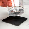 Hand hält ein Glas, das auf einem schwarzen Untersetzer steht