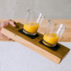 Hand hält ein Holzbrett mit zwei Gläsern Orangensaft