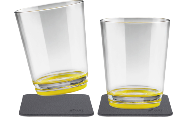 Zwei transparente Gläser mit gelbem Boden, eines steht schräg, das andere aufrecht, beide auf schwarzen Untersetzern