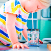 Kind in farbig gestreiftem T-Shirt trinkt Wasser aus einem Glas mit Strohhalm