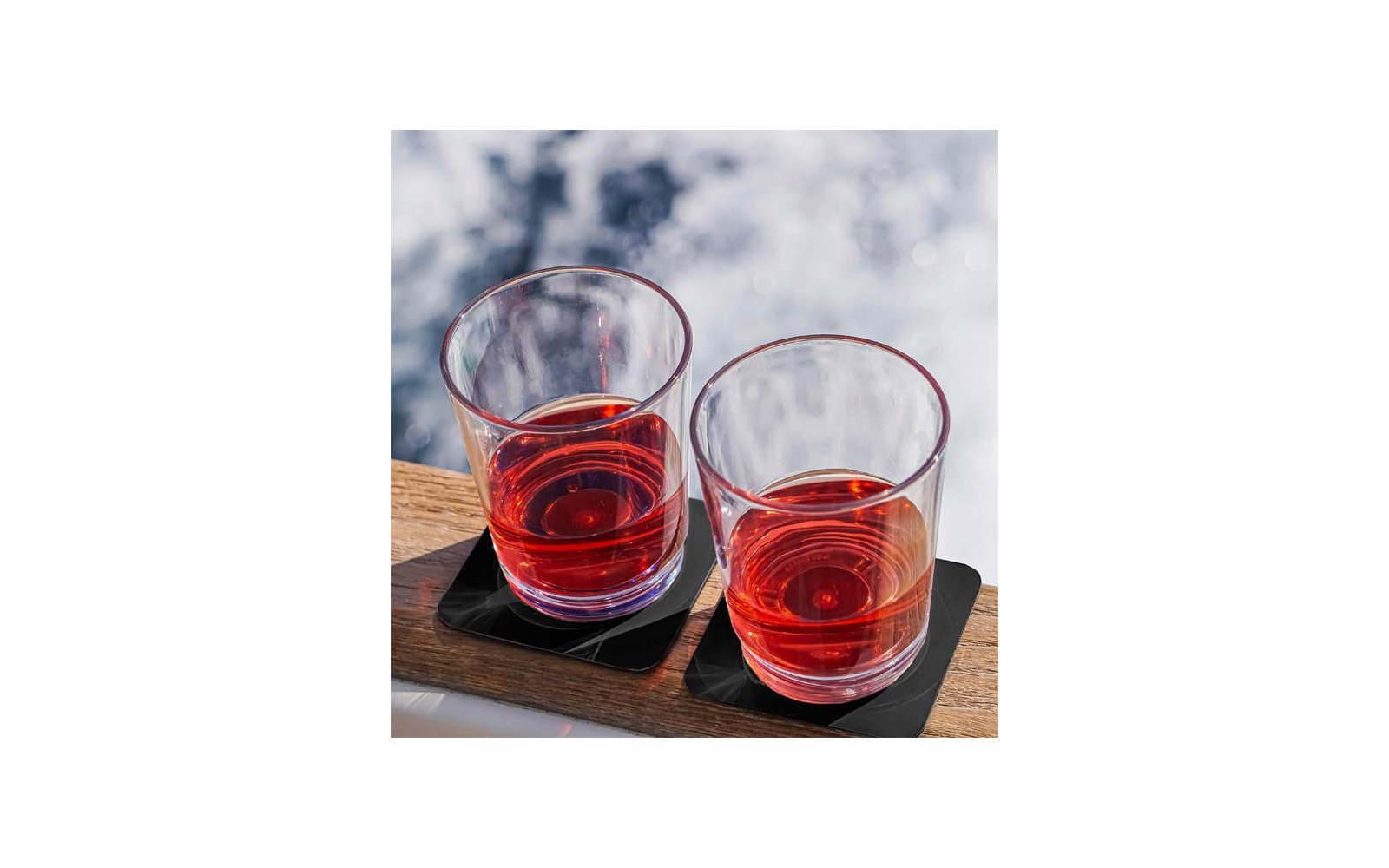 Zwei Glasbecher mit rotem Getränk auf einem Holzbrett vor unscharfem Hintergrund