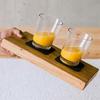 Hand hält ein Holzbrett mit zwei Gläsern Orangensaft