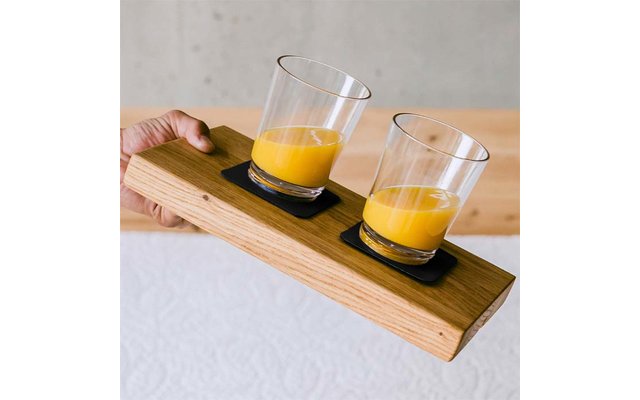 Hand hält ein Holzbrett mit zwei Gläsern Orangensaft