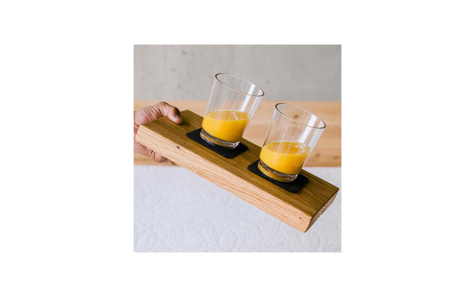 Hand hält ein Holzbrett mit zwei Gläsern Orangensaft