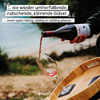 Person gießt roten Wein aus einer Flasche in ein Glas, das auf einem runden Holztablett steht, draußen am Wasser