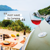 Glas mit rotem Wein auf einem grünen Zelt mit Meer und Landschaft im Hintergrund