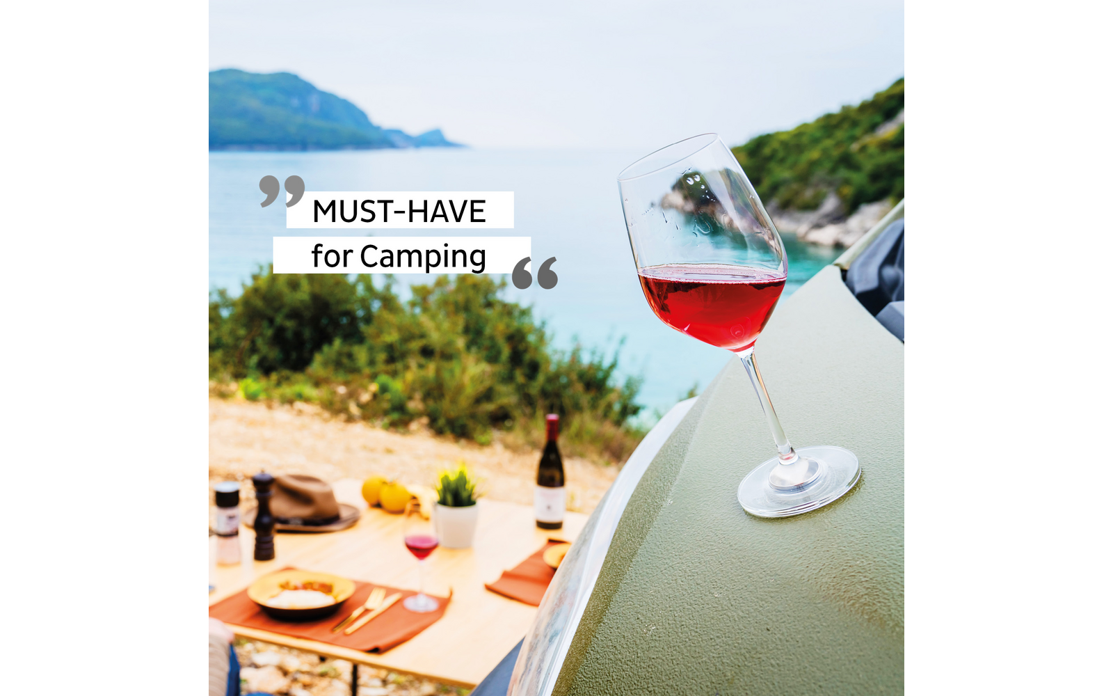 Glas mit rotem Wein auf einem grünen Zelt mit Meer und Landschaft im Hintergrund