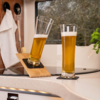 Zwei Biergläser, eines geneigt auf einem Holzhalter, das andere stehend auf einer Küchenarbeitsplatte