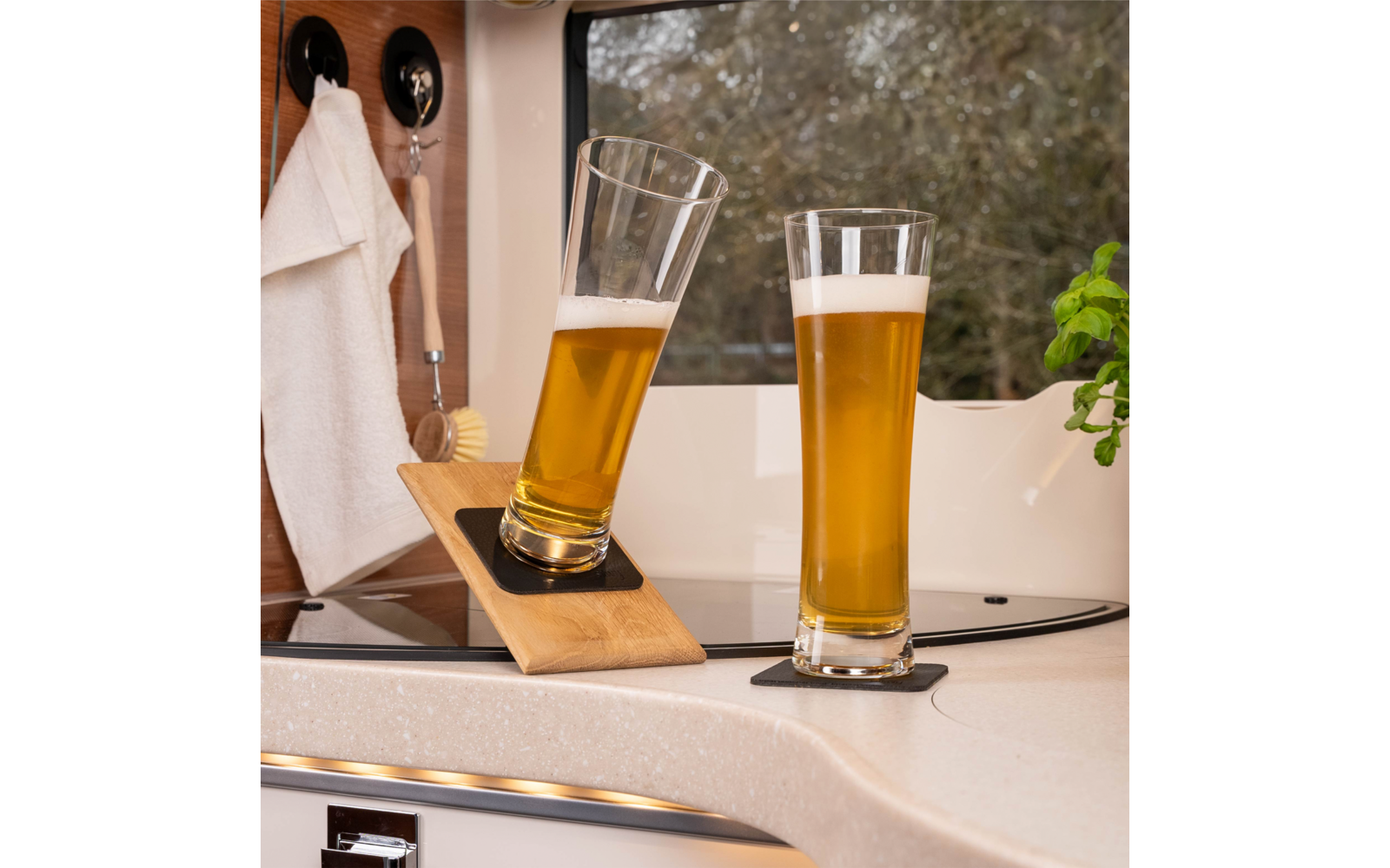 Zwei Biergläser, eines geneigt auf einem Holzhalter, das andere stehend auf einer Küchenarbeitsplatte