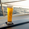 Glas mit Bier auf dem Rand eines Boots mit Meer im Hintergrund