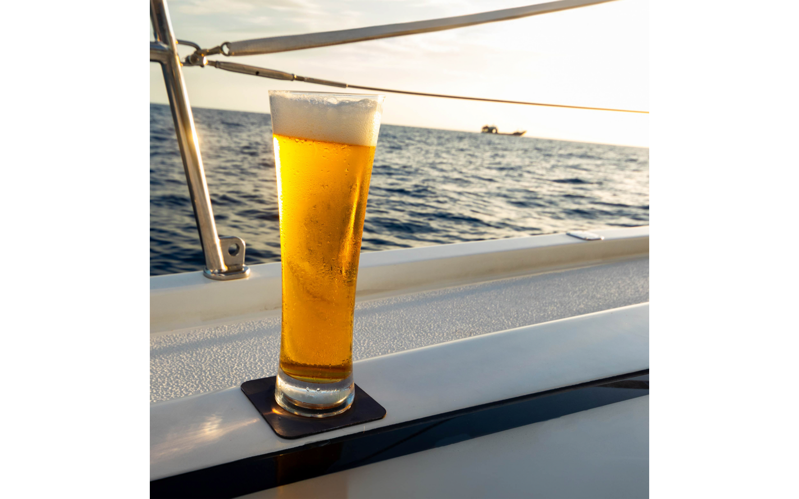 Glas mit Bier auf dem Rand eines Boots mit Meer im Hintergrund