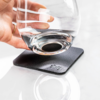 Main posant un verre sur un dessous de verre noir sur un fond clair