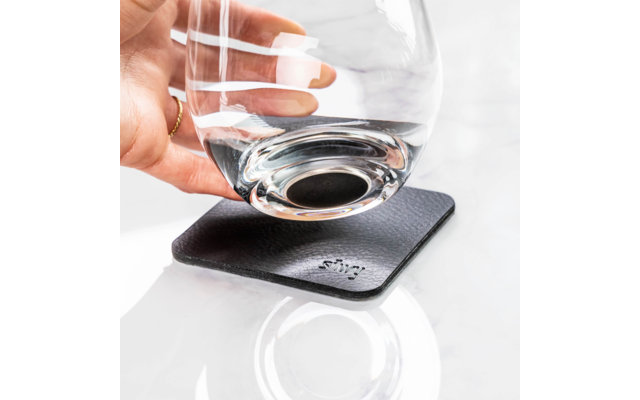 Main posant un verre sur un dessous de verre noir sur un fond clair