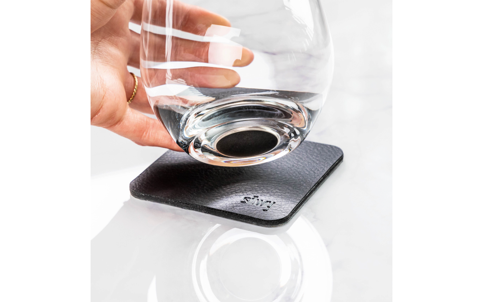 Main posant un verre sur un dessous de verre noir sur un fond clair
