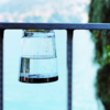 Omgekeerd drinkglas met water op een metalen reling, wazig meer en bomen op de achtergrond