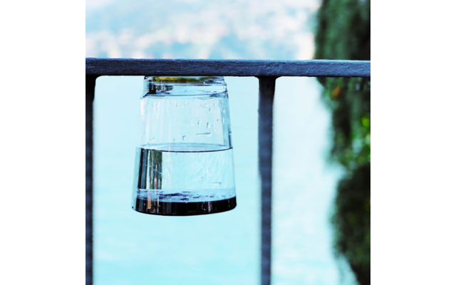 Omgekeerd drinkglas met water op een metalen reling, wazig meer en bomen op de achtergrond