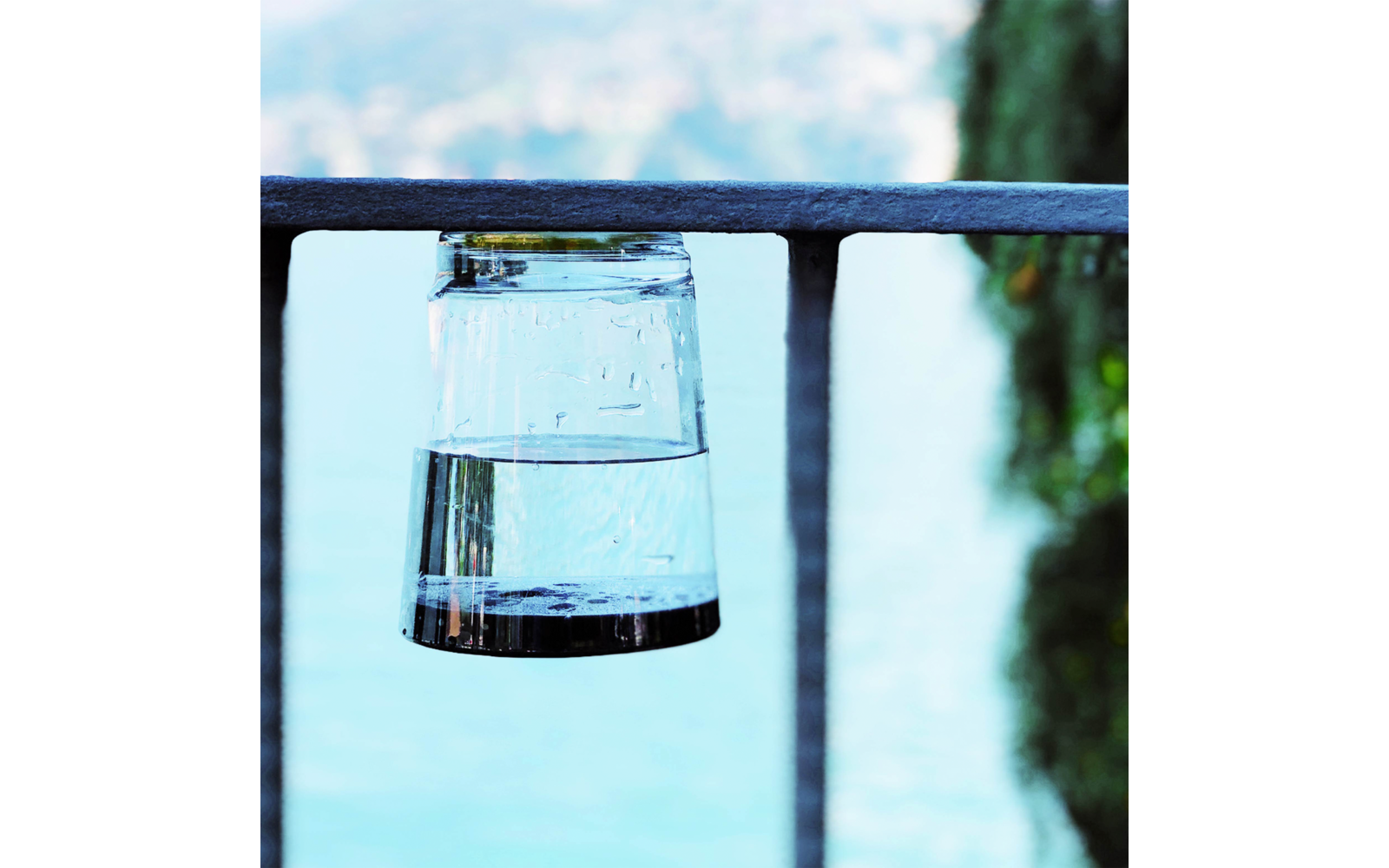Omgekeerd drinkglas met water op een metalen reling, wazig meer en bomen op de achtergrond