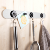Metal strip with four hooks mounted on a wooden panel, holding a whisk, a note, a ladle, and a gray dish towel
