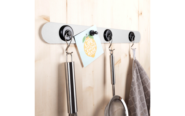 Metal strip with four hooks mounted on a wooden panel, holding a whisk, a note, a ladle, and a gray dish towel
