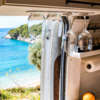 Wine glasses hanging in a camper in front of an open window overlooking the sea and a wooded hill