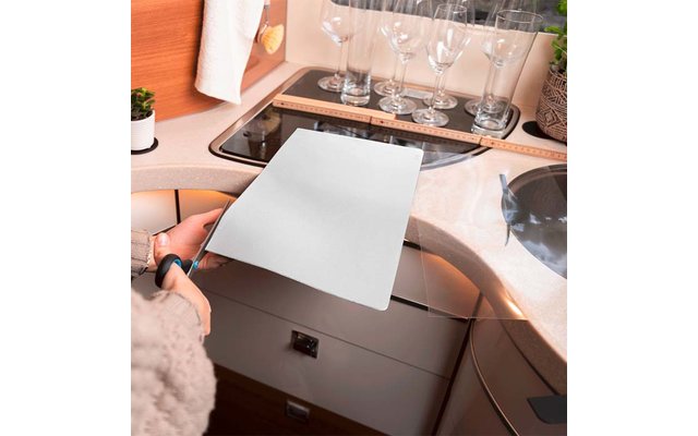 Eine Person schneidet mit einer Schere ein weißes Blatt Papier auf einer Küchenarbeitsplatte