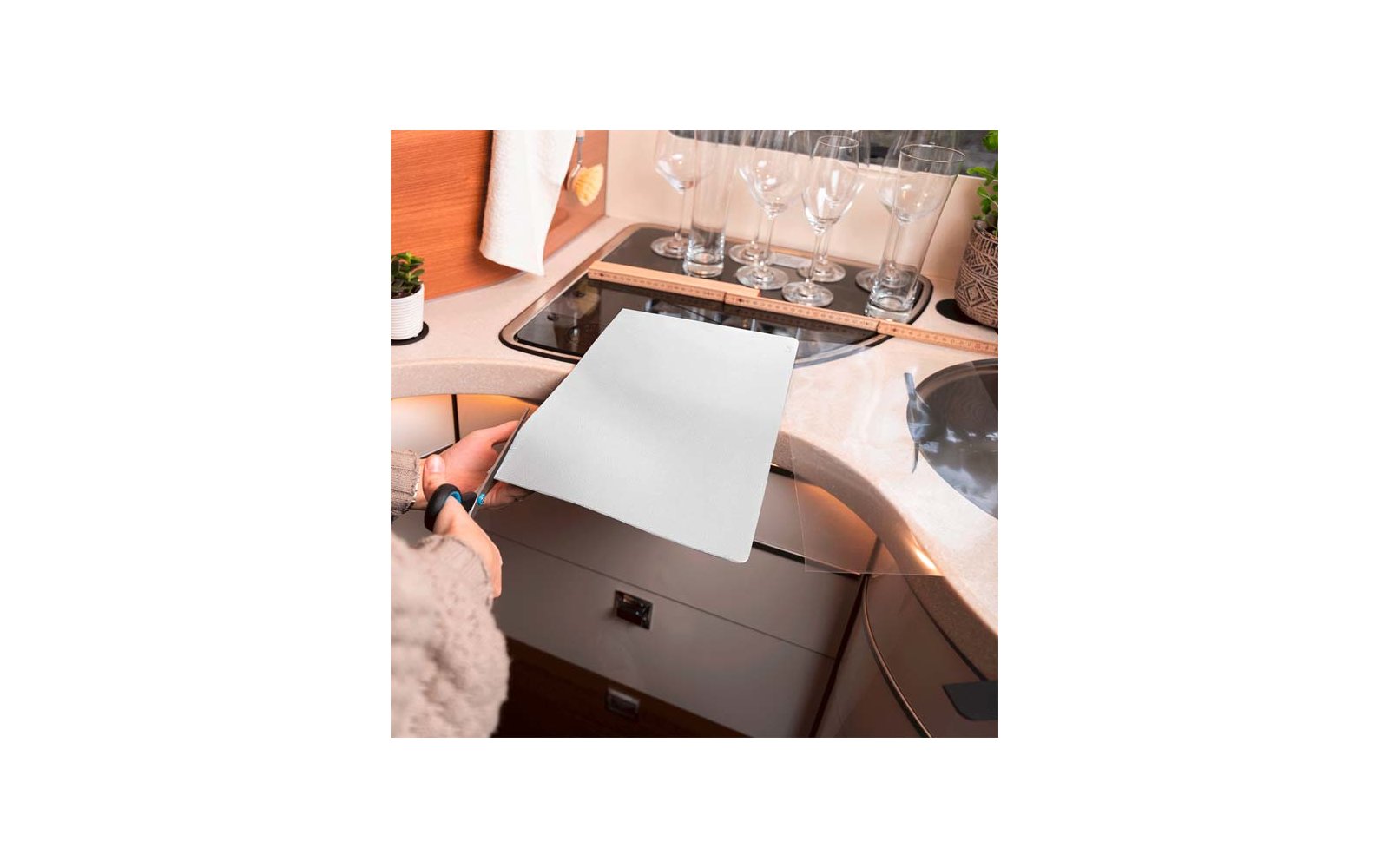 Eine Person schneidet mit einer Schere ein weißes Blatt Papier auf einer Küchenarbeitsplatte