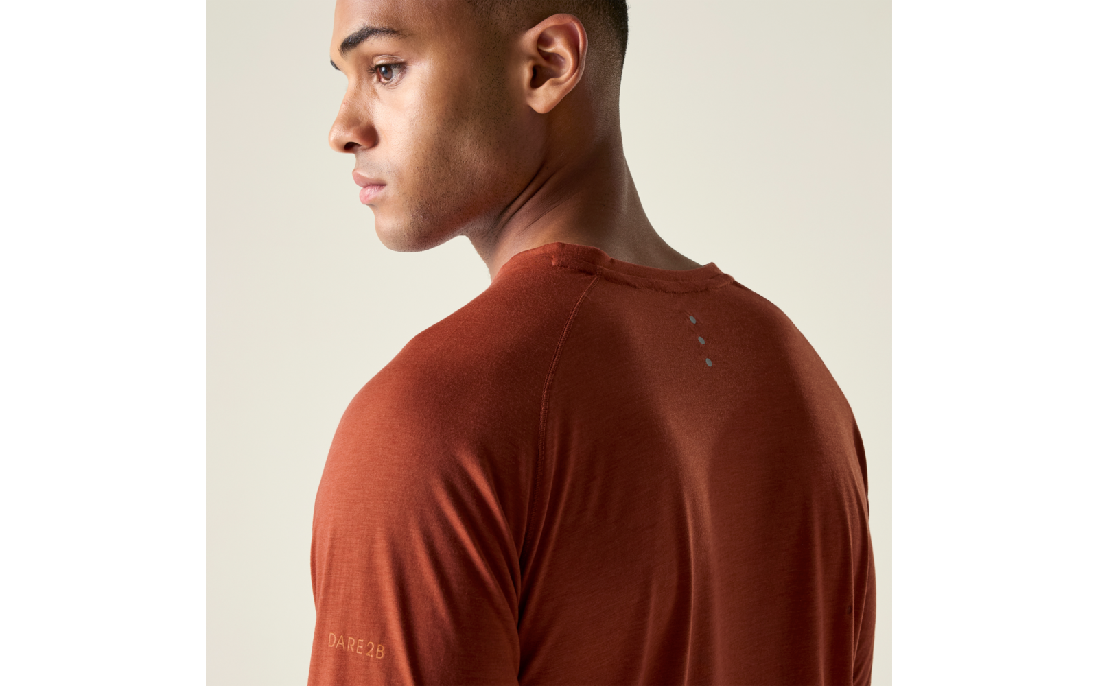 Seitliches Porträt einer Person mit kurzem dunklem Haar, die ein rostbraunes T-Shirt trägt, vor hellem Hintergrund