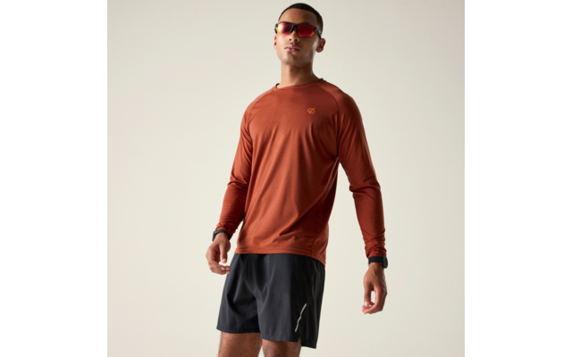 Person steht vor hellem Hintergrund, trägt rostfarbenes Langarmshirt, schwarze Shorts und rote verspiegelte Sonnenbrille