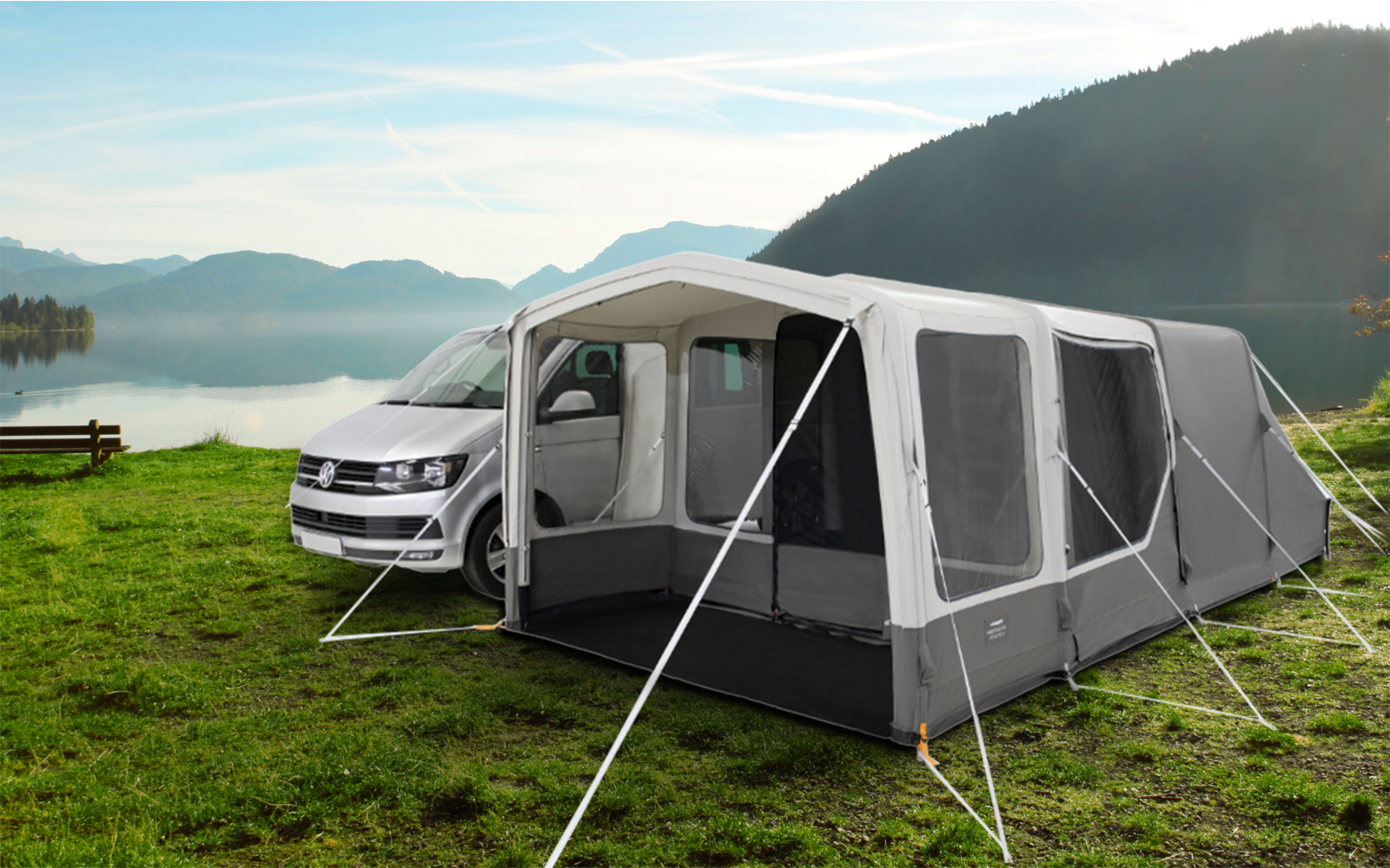 Campingplatz mit einem weißen Wohnmobil und einem grauen Vorzelt am See, umgeben von Bergen