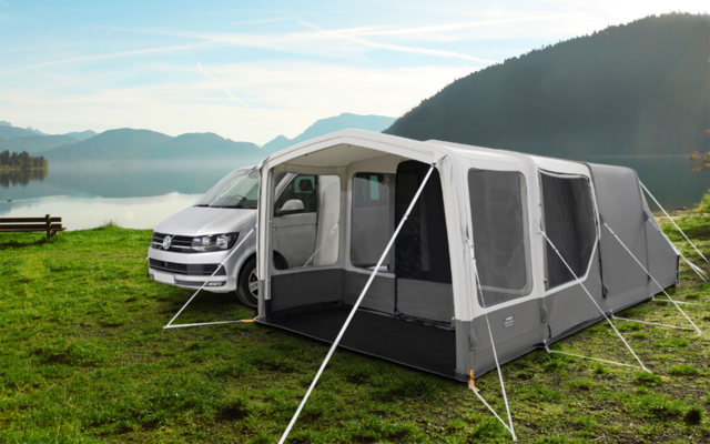 Campingplatz mit einem weißen Wohnmobil und einem grauen Vorzelt am See, umgeben von Bergen