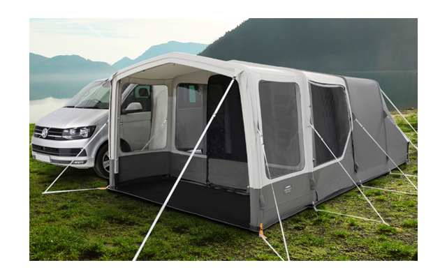 Campingplatz mit einem weißen Wohnmobil und einem grauen Vorzelt am See, umgeben von Bergen