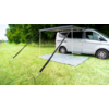White camper van with extended awning on a grassy area next to trees
