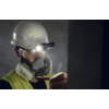 Person mit Schutzhelm, Maske und Stirnlampe in dunkler Umgebung
