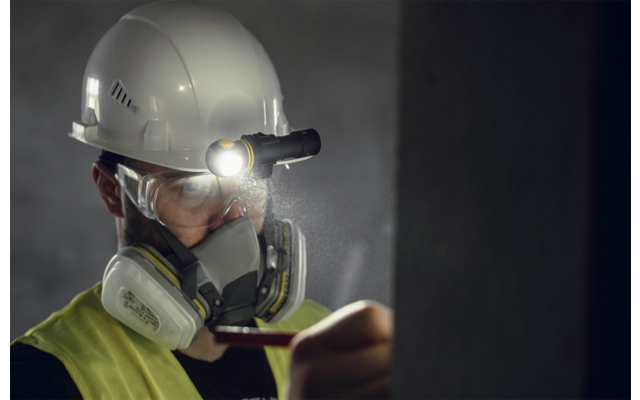 Person mit Schutzhelm, Maske und Stirnlampe in dunkler Umgebung