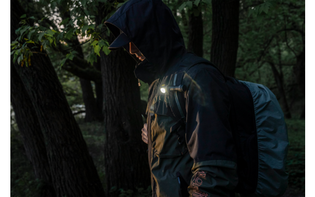Person mit Kapuzenjacke und Rucksack im Wald bei schwachem Licht