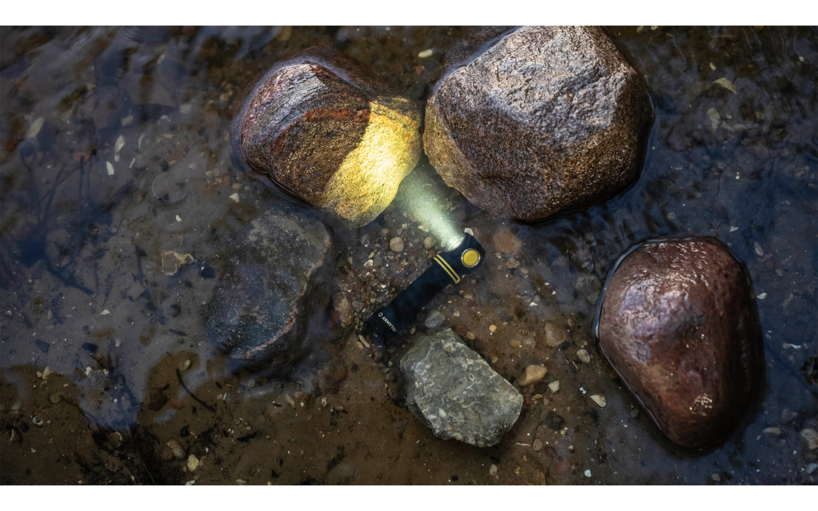 Mehrere Steine liegen im Wasser, eine Taschenlampe liegt zwischen den Steinen