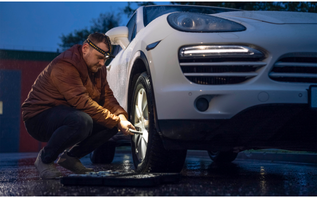 Ein Mann prüft den Reifen eines weißen Autos bei Dämmerung