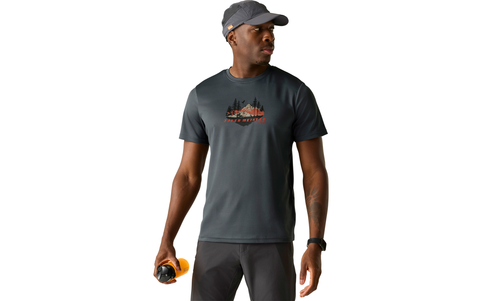 Mann mit grauer Kappe, dunklem T‑Shirt mit Berggrafik und dunkler Hose, hält eine gelbe Trinkflasche in einer Hand