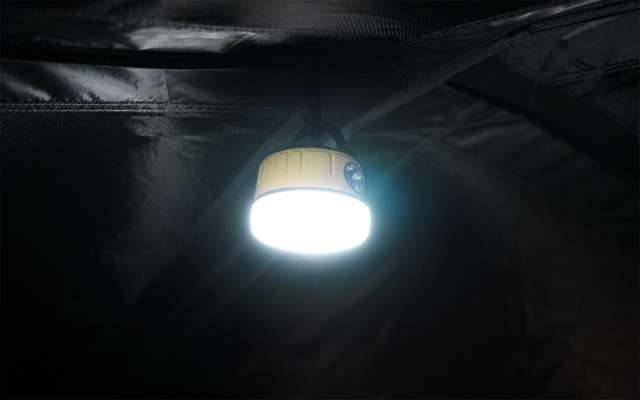 Runde, hängende Leuchte mit hellem weißem Licht, an einem Kabel befestigt vor dunklem Stoffhintergrund