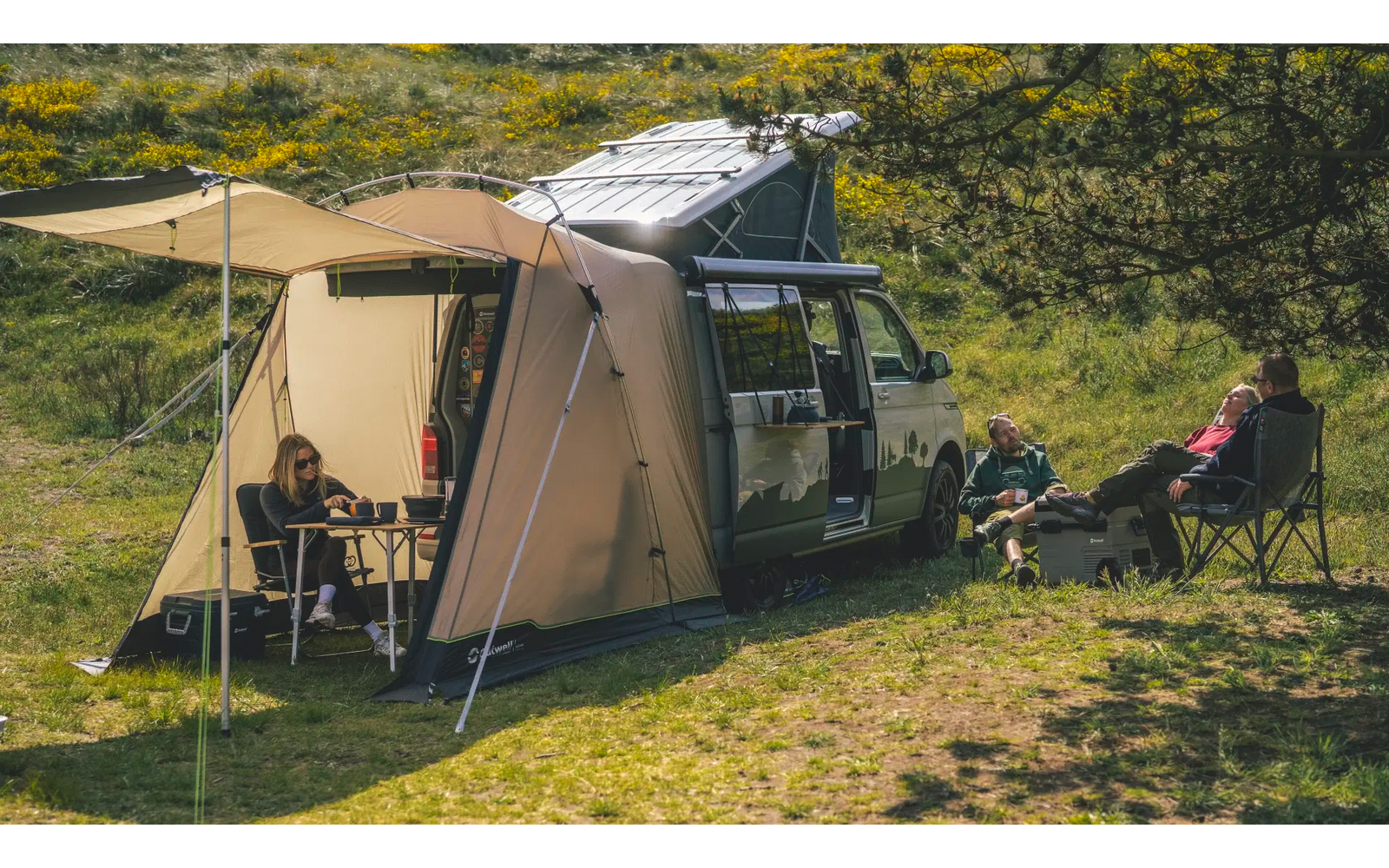 Zelt und Wohnmobil auf einer Wiese mit zwei Personen auf Campingstühlen