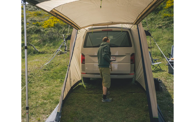 Person steht in einem offenen kleinen Zelt, grüner Hügel im Hintergrund
