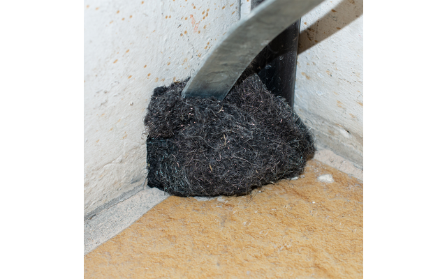 Schep met zwart zand of aarde in een hoek van een kamer op een lichte vloer