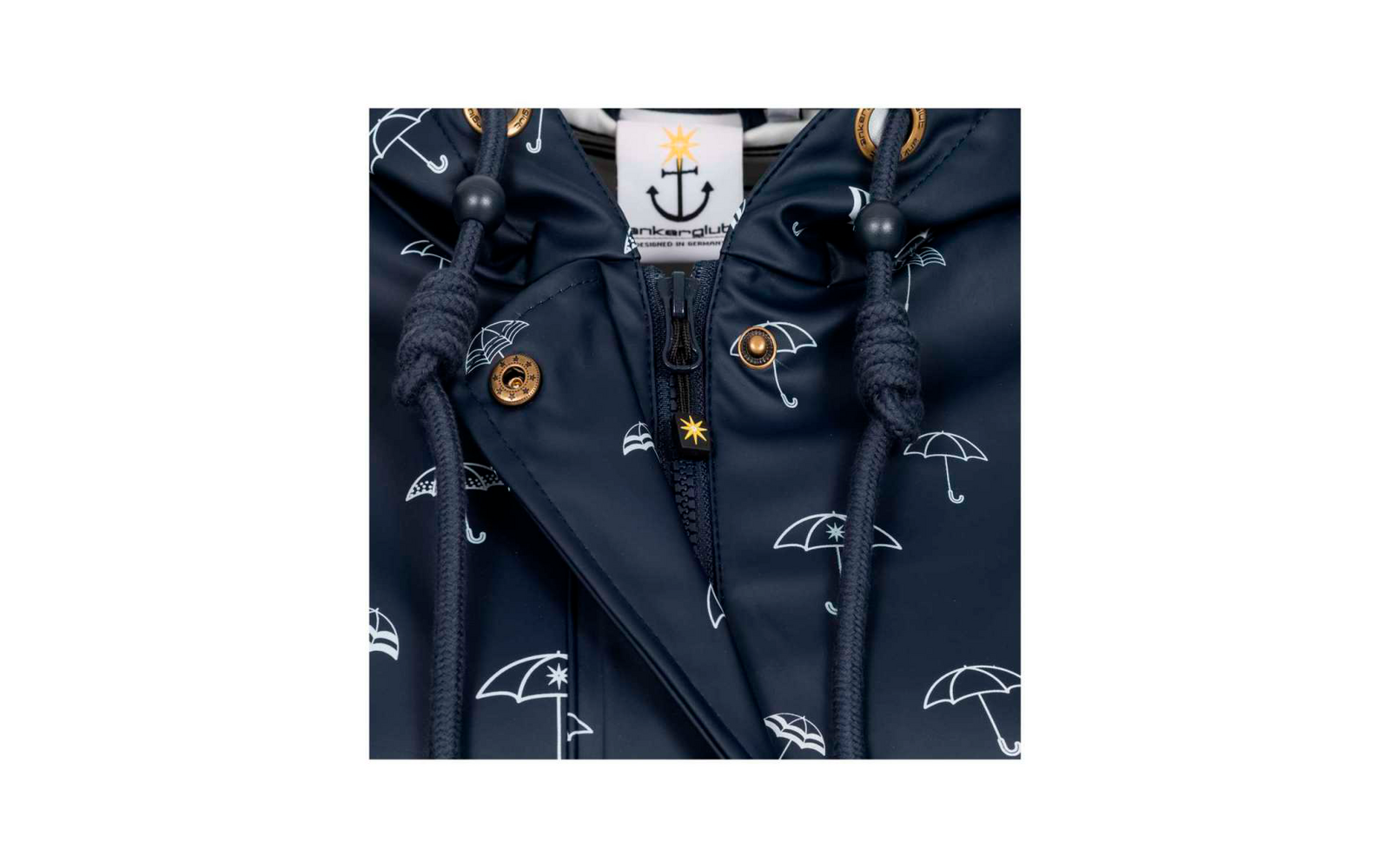 Donkerblauwe jas met wit paraplu‑patroon, centrale rits, koord met stopper, goudkleurige drukknop en wit label met ankerlogo en gele ster
