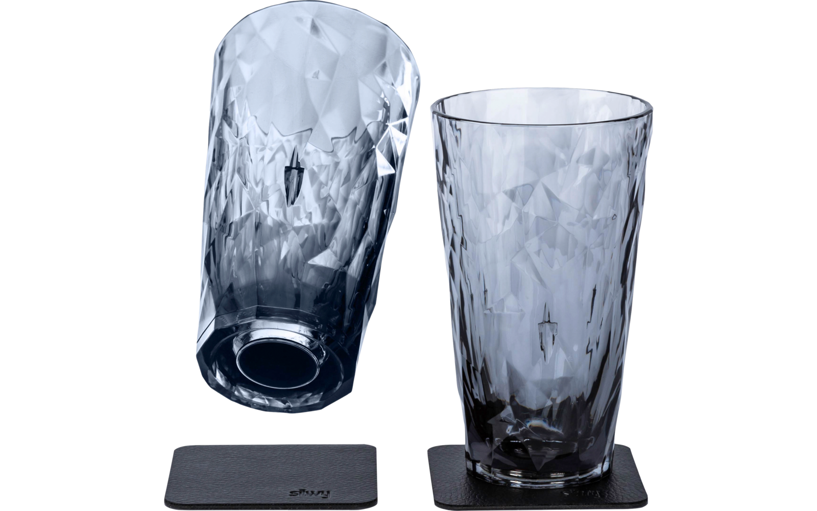 Zwei facettierte graue Trinkgläser und zwei quadratische schwarze Untersetzer; ein Glas steht rechts auf einem Untersetzer, das andere liegt links schräg auf einem zweiten Untersetzer