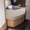 Lit rond avec drap beige, oreiller gris et blanc dans une petite pièce avec des meubles en bois
