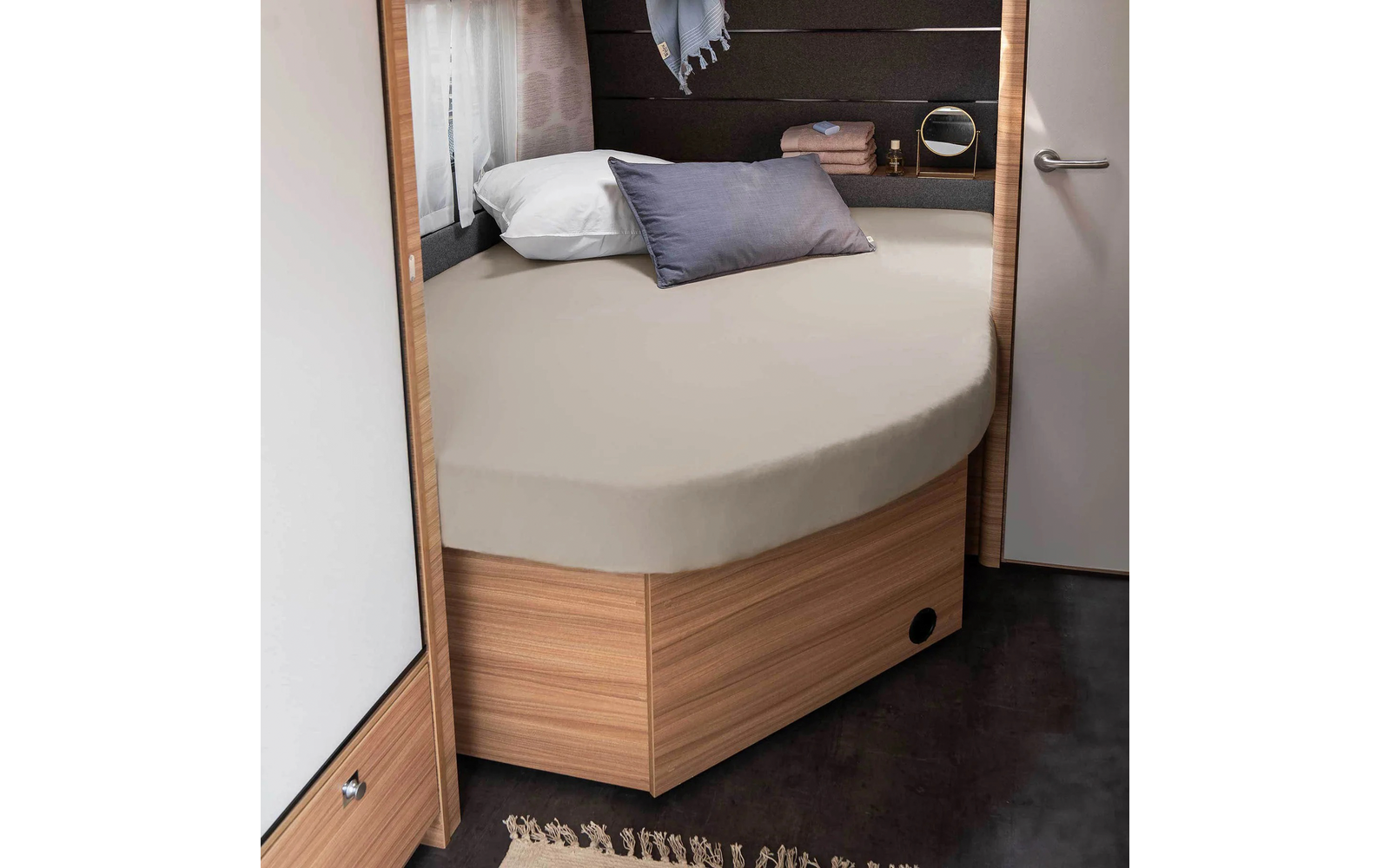 Lit rond avec drap beige, oreiller gris et blanc dans une petite pièce avec des meubles en bois