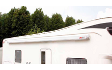 Partial view of a white motorhome with extended awning, trees in the background