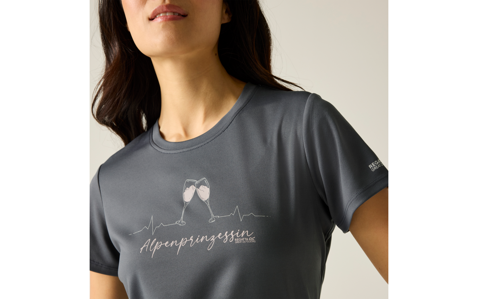Haut du corps d'une personne portant un t‑shirt gris à encolure ronde, imprimé de deux verres qui s'entrechoquent, motif de ligne de battement cardiaque et inscription "Alpenprinzessin", petit logo sur la manche