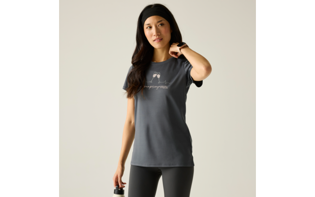 Femme aux longs cheveux foncés portant un bandeau noir et un T‑shirt sombre à manches courtes avec petit imprimé blanc, leggings noirs, tenant une bouteille d'eau dans la main gauche, main droite au niveau du cou, fond uni clair